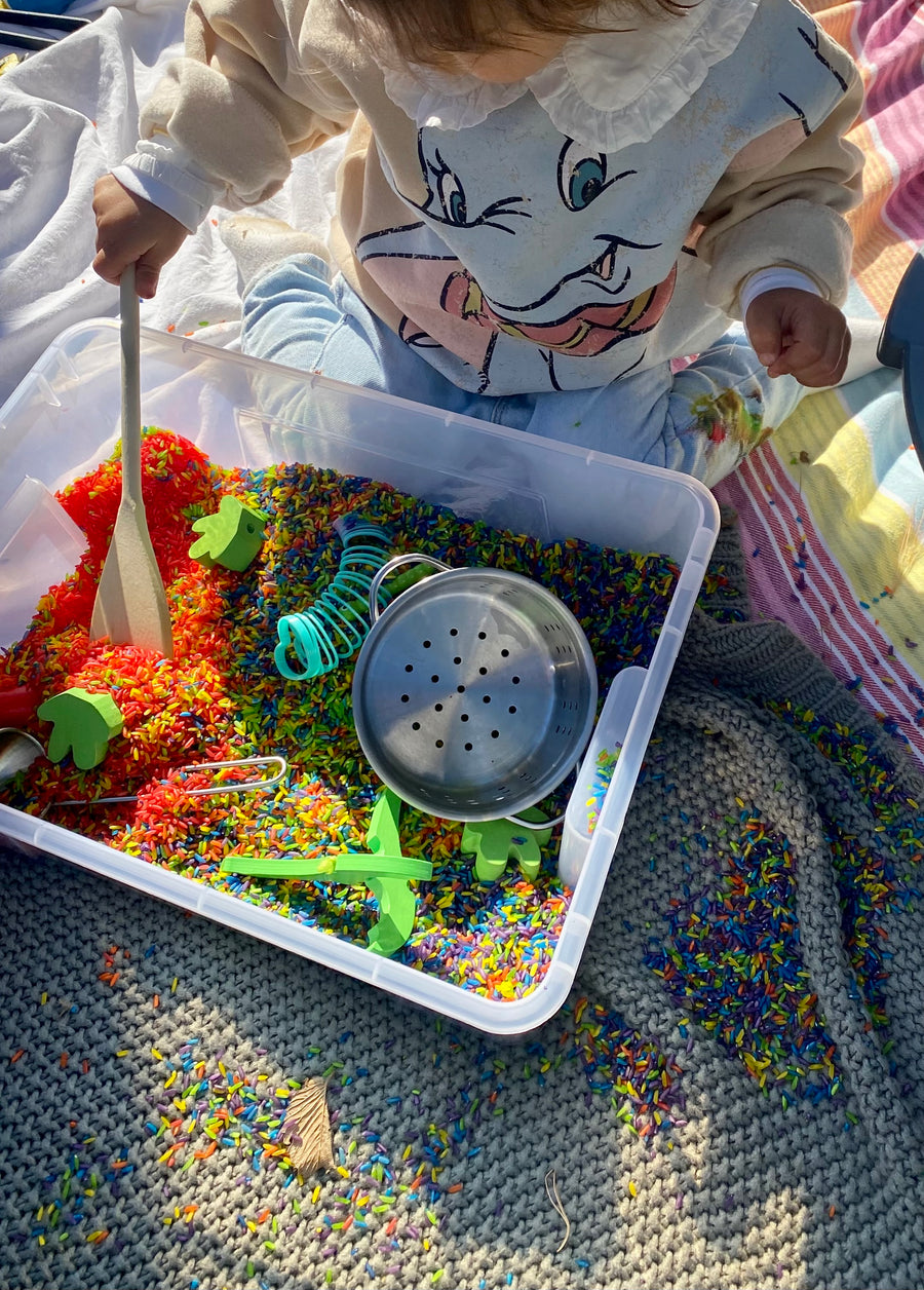 Toddler playing in a sensory bin of rainbow-coloured rice