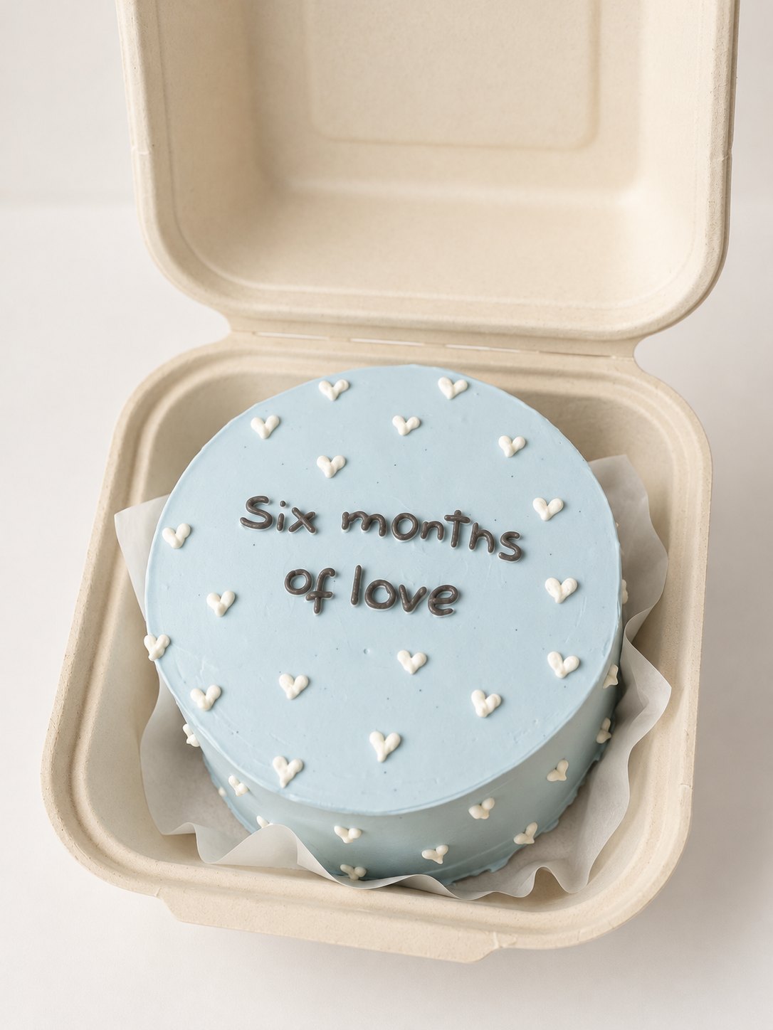 Small blue bento box cake with piped white hearts and a six months of love message