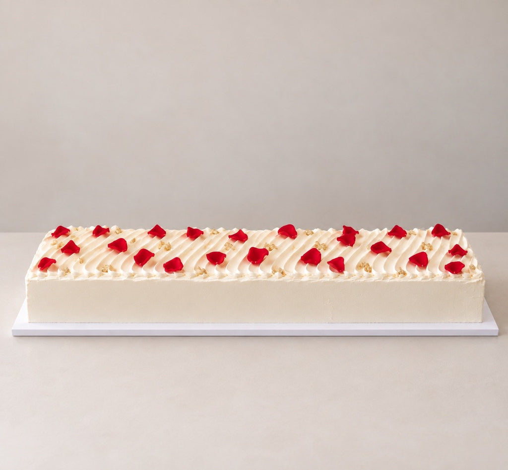 Long rectangular celebration cake with piped ridges and red rose petals