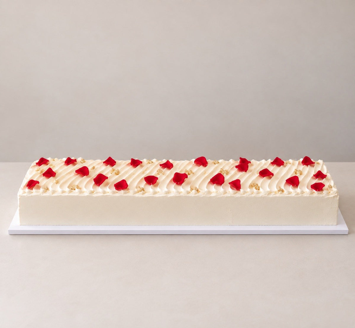 Long rectangular celebration cake with piped ridges and red rose petals